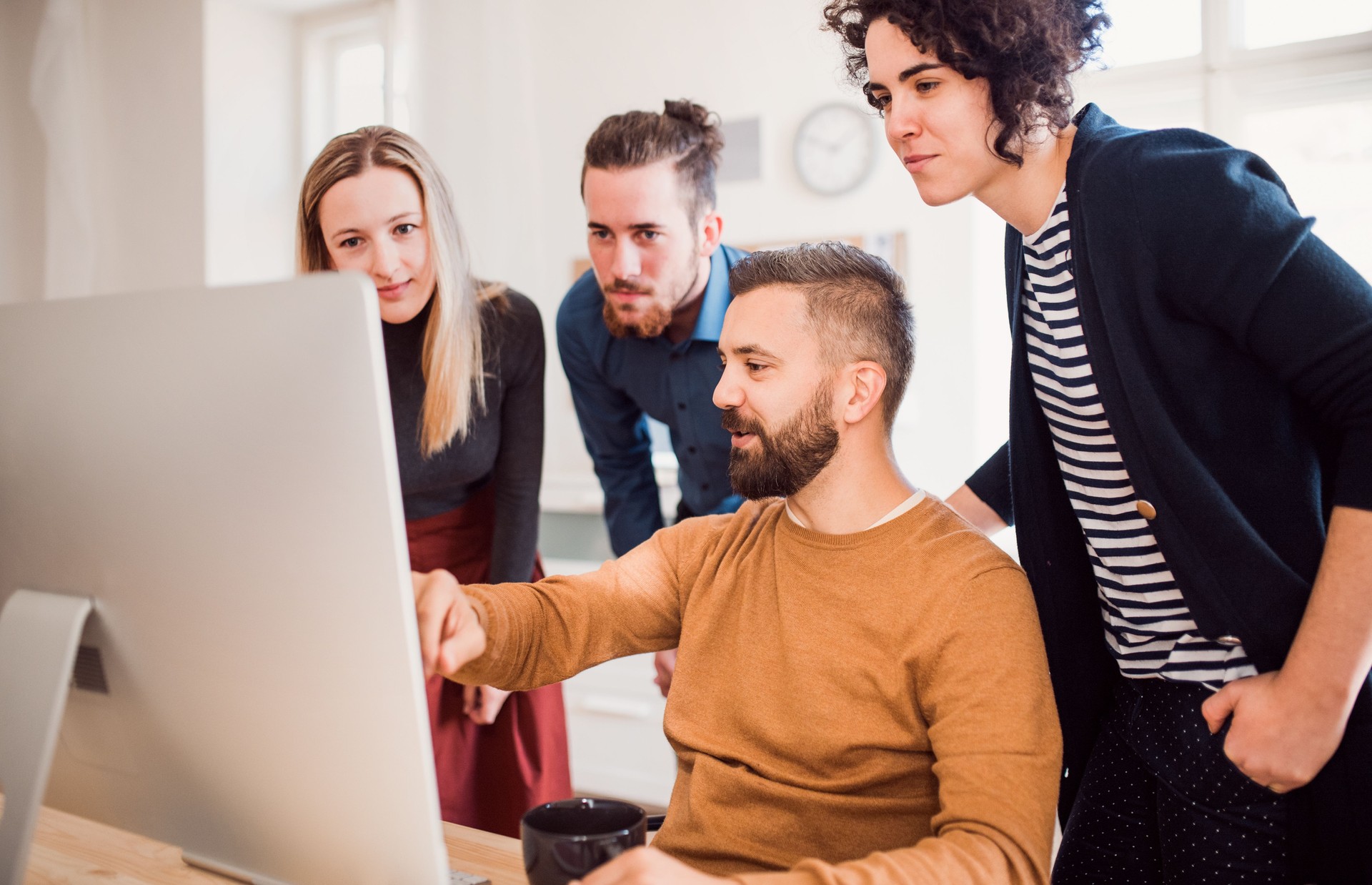 Group of young businesspeople looking at laptop screen in office, discussing issues.