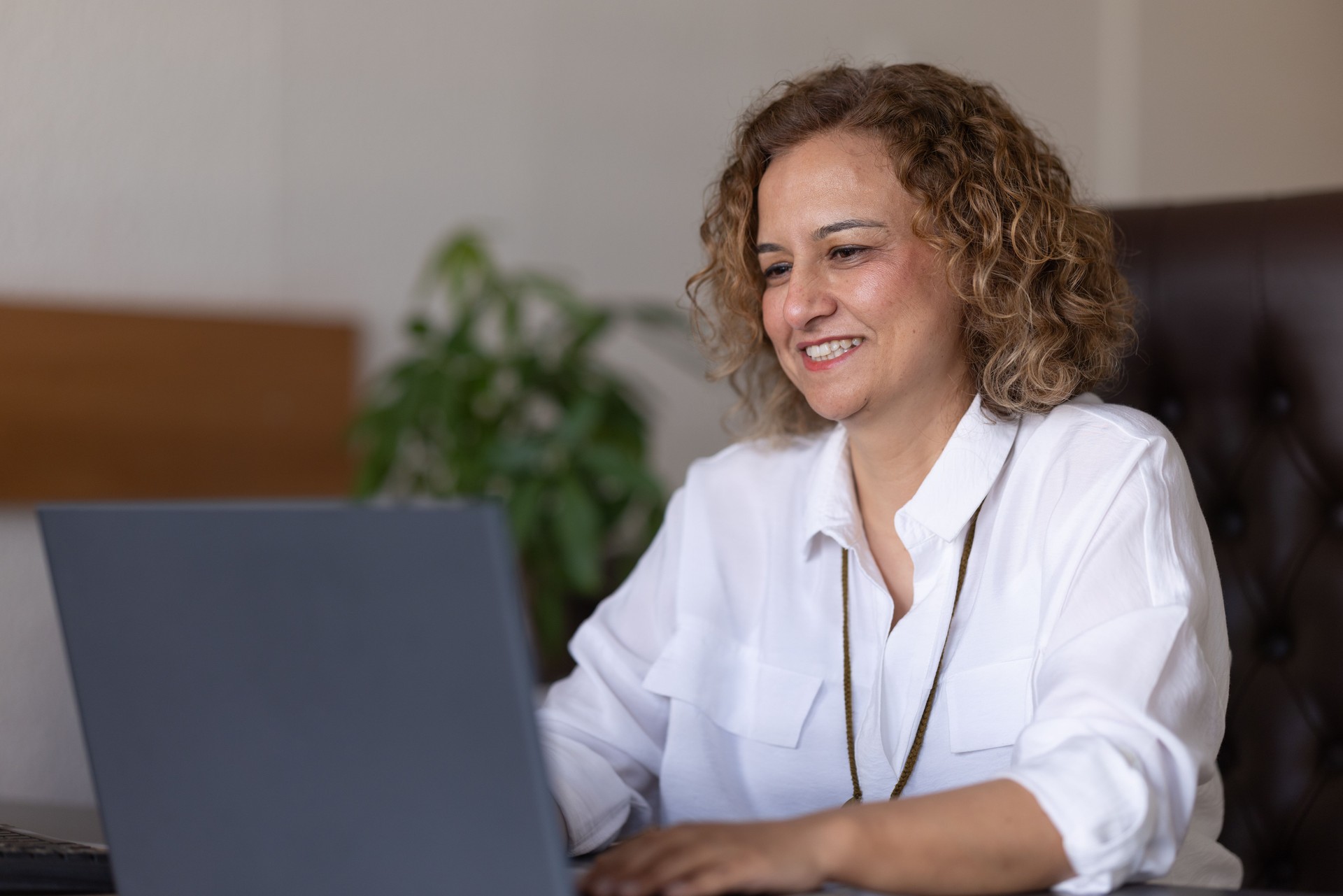 Middle-aged businesswoman using laptop and smiling in her modern office